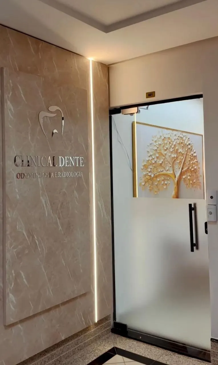 Entrada com parede de mármore iluminada e porta de vidro jateado, com quadro de árvore dourada ao fundo